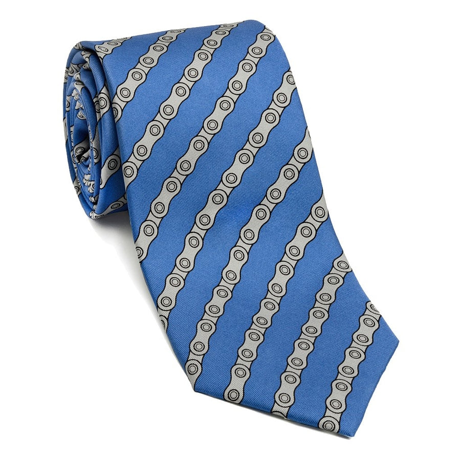 A silk necktie with a pattern resembling a bike chain, primarily blue with grayish-white elements, laid out on a flat surface.