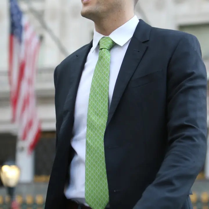 Man wearing a dark suit with a green tie in an outdoor setting