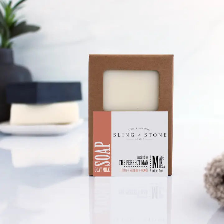 Bar of woods, amber, and citrus scented goat milk soap in a cardboard box with 'Sling & Stone' branding on a white background