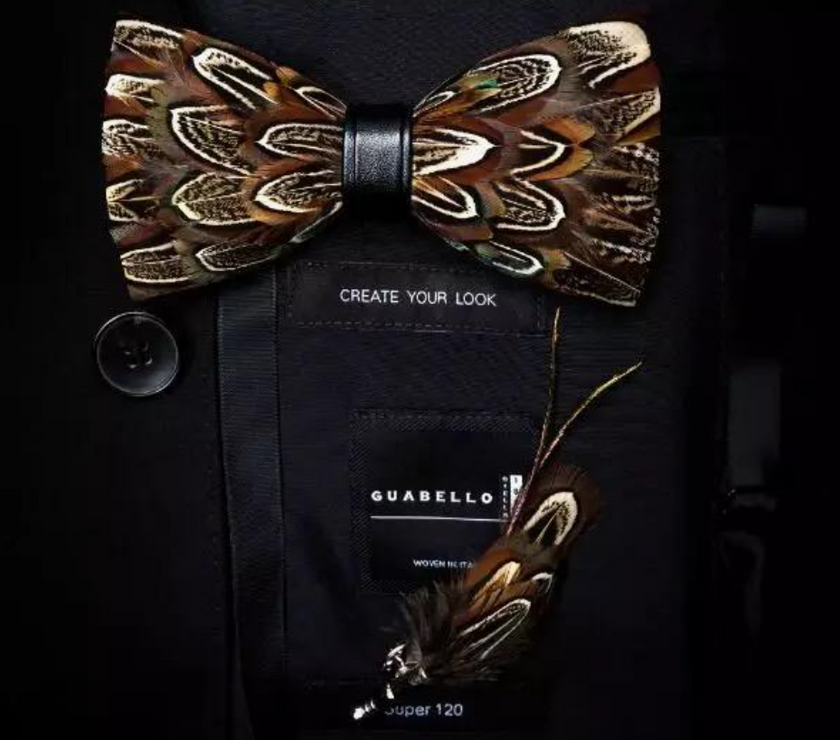A handmade brown feather bow tie on top of a bag that says "create your look" with another feather accent below.