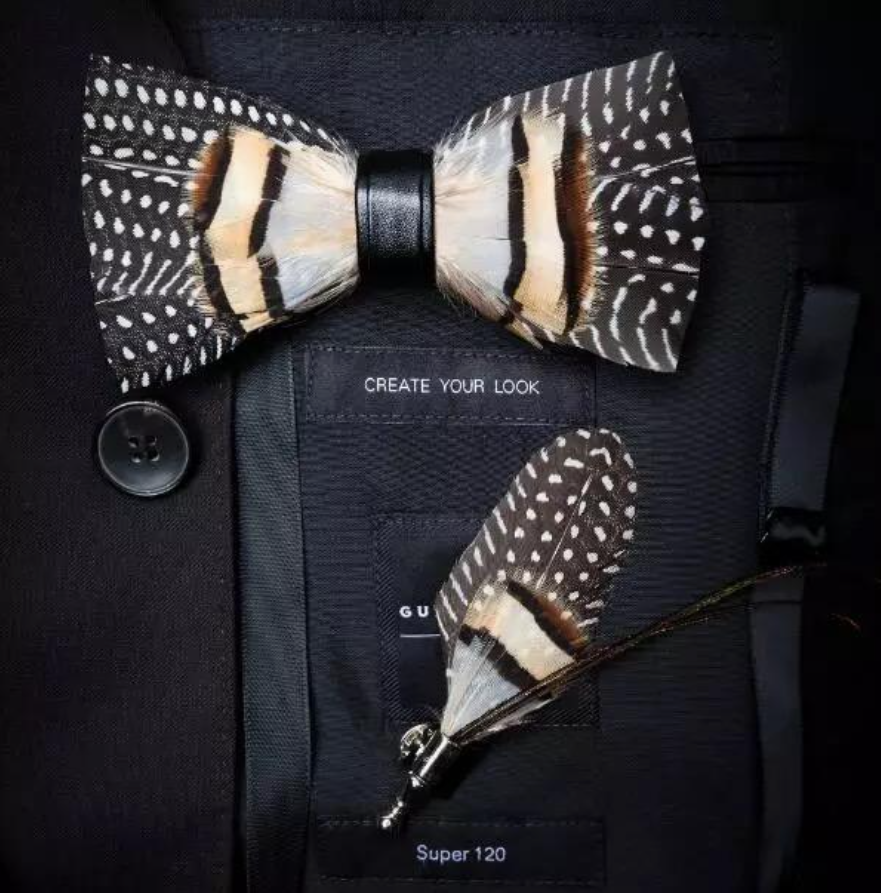 A handmade brown and white feather bow tie on a bag that says "create your look" with another feather accent below.