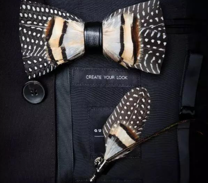 A handmade brown and white feather bow tie on a bag that says "create your look" with another feather accent below.