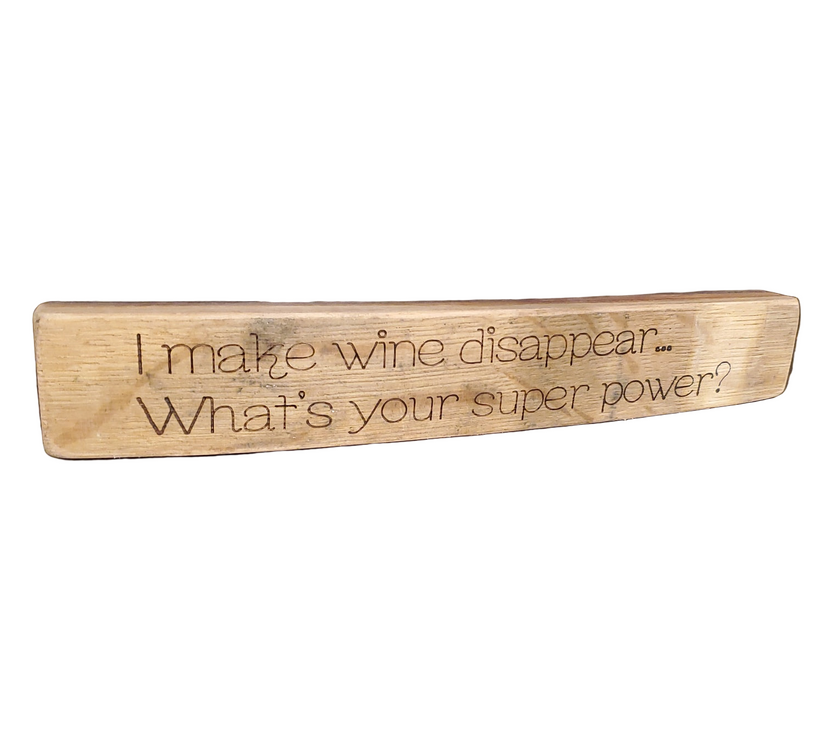 Wooden block with engraved text 'I make wine disappear... What's your super power?' on a white background