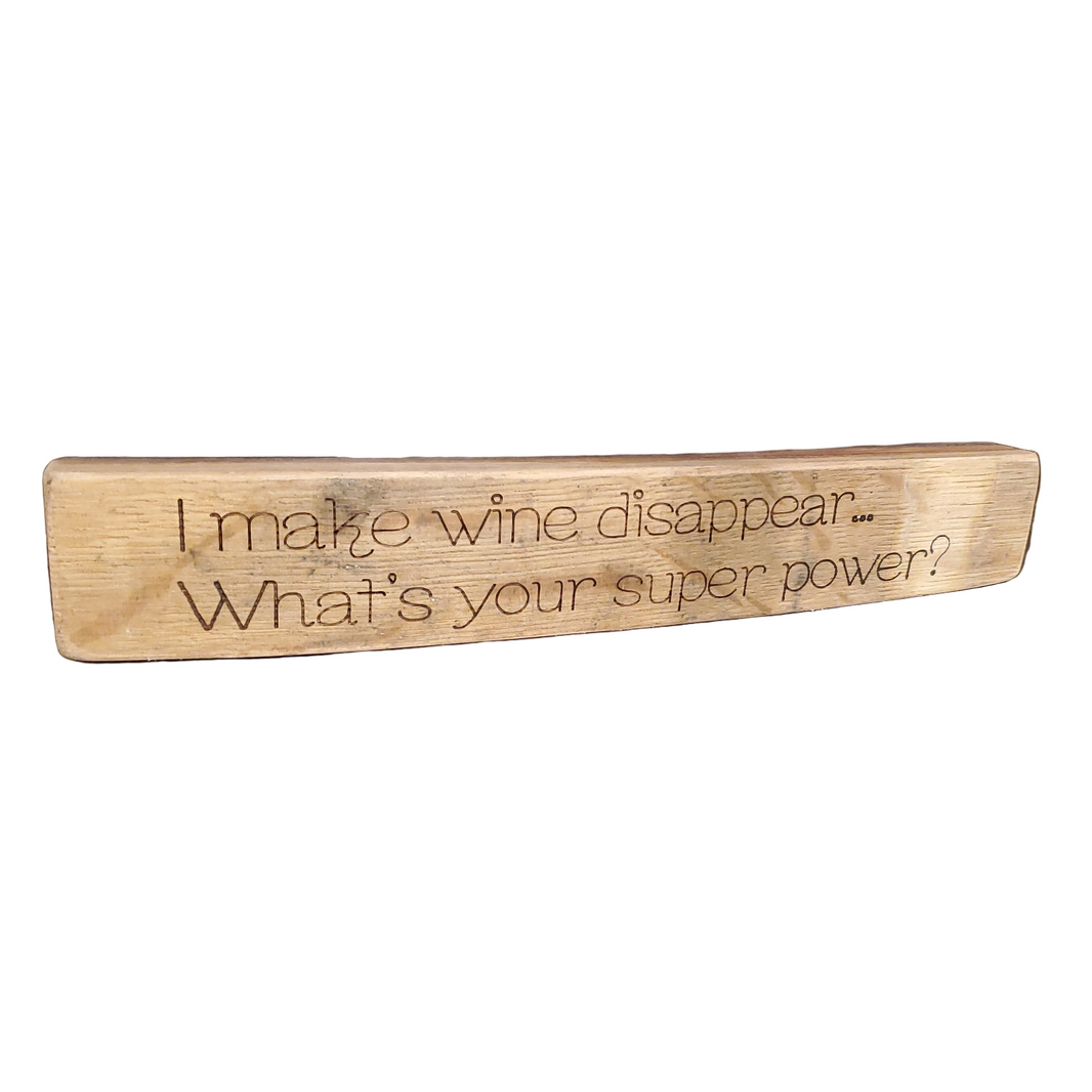 Wooden block with engraved text 'I make wine disappear... What's your super power?' on a white background