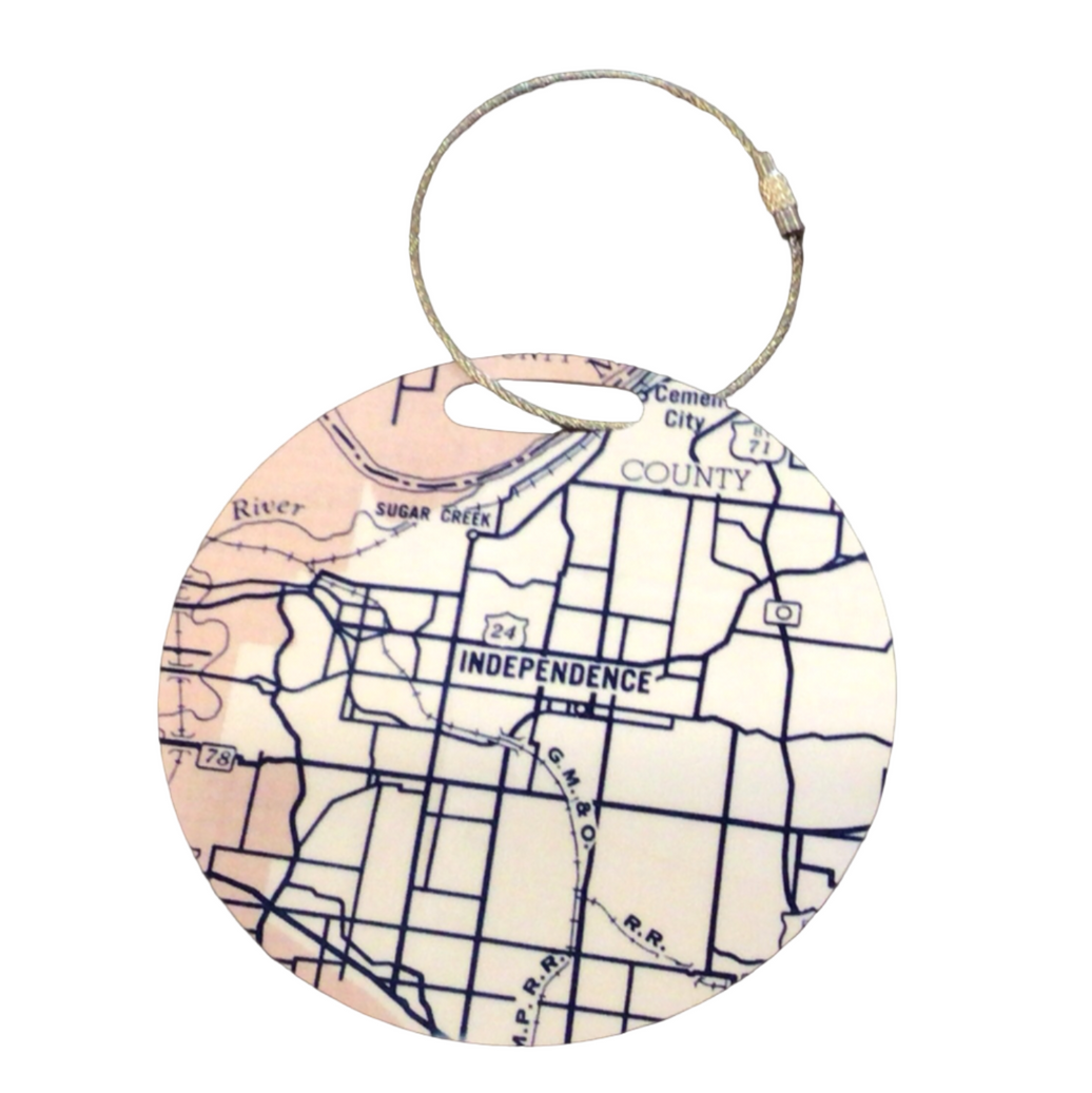 A round luggage tag with a map of Independence, Missouri on it, attached to a durable cable attachment.