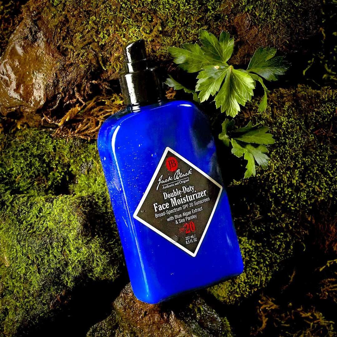 A blue bottle of Jack Black Double Duty Face Moisturizer with SPF 20 with black labeling on a mossy rock.