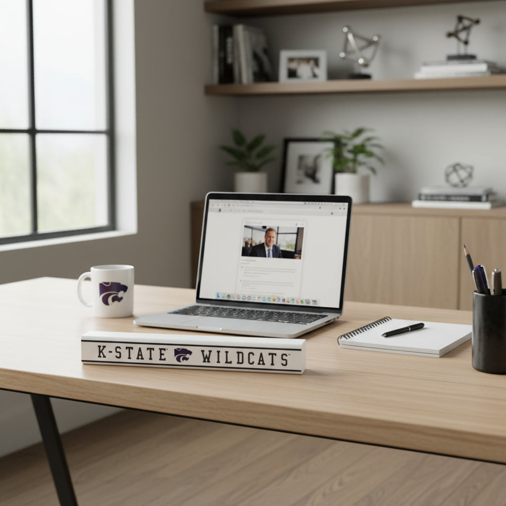 A rectangular pine wood sign with 'K-State Wildcats' text, placed on a desk with a computer and coffee mug and other office items in the background.