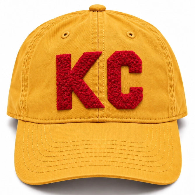 A yellow cotton baseball cap featuring large, textured red letters 'KC' embroidered on the front, set against a plain white background.