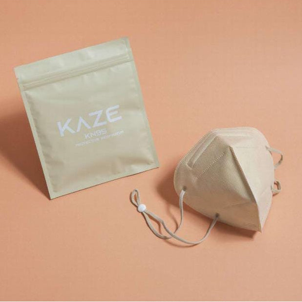 A beige KAZE KN95 face mask with packaging on a peach colored background