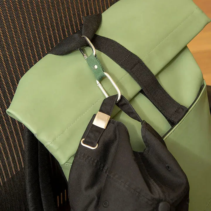 Green backpack with black strap and dual-clip attached to backpack and a hat.