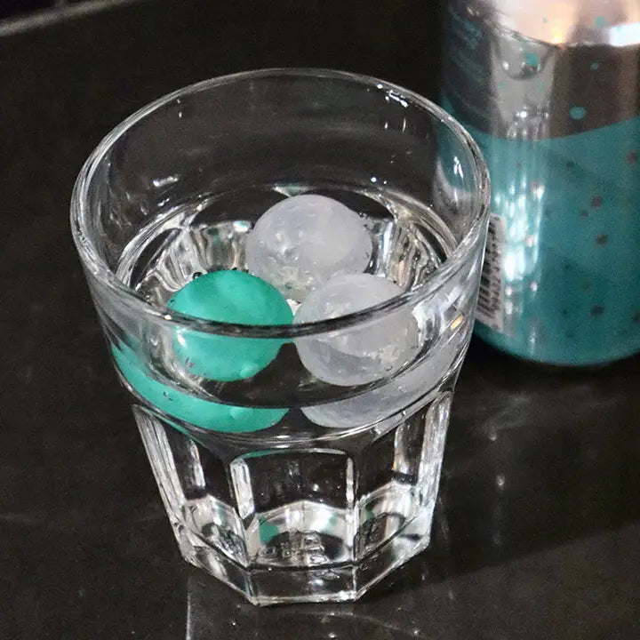Clear glass with golf ball shaped ice cubes in teal and clear colors.