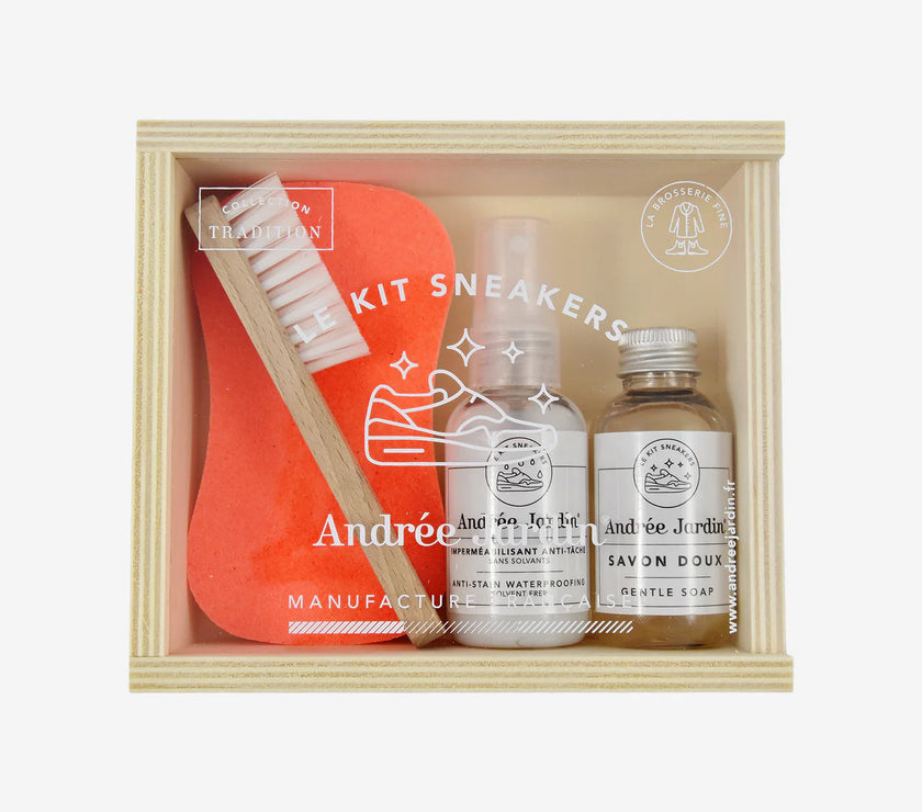 Shoe cleaning kit with a brush, bottle, and jar in a wooden box on a white background