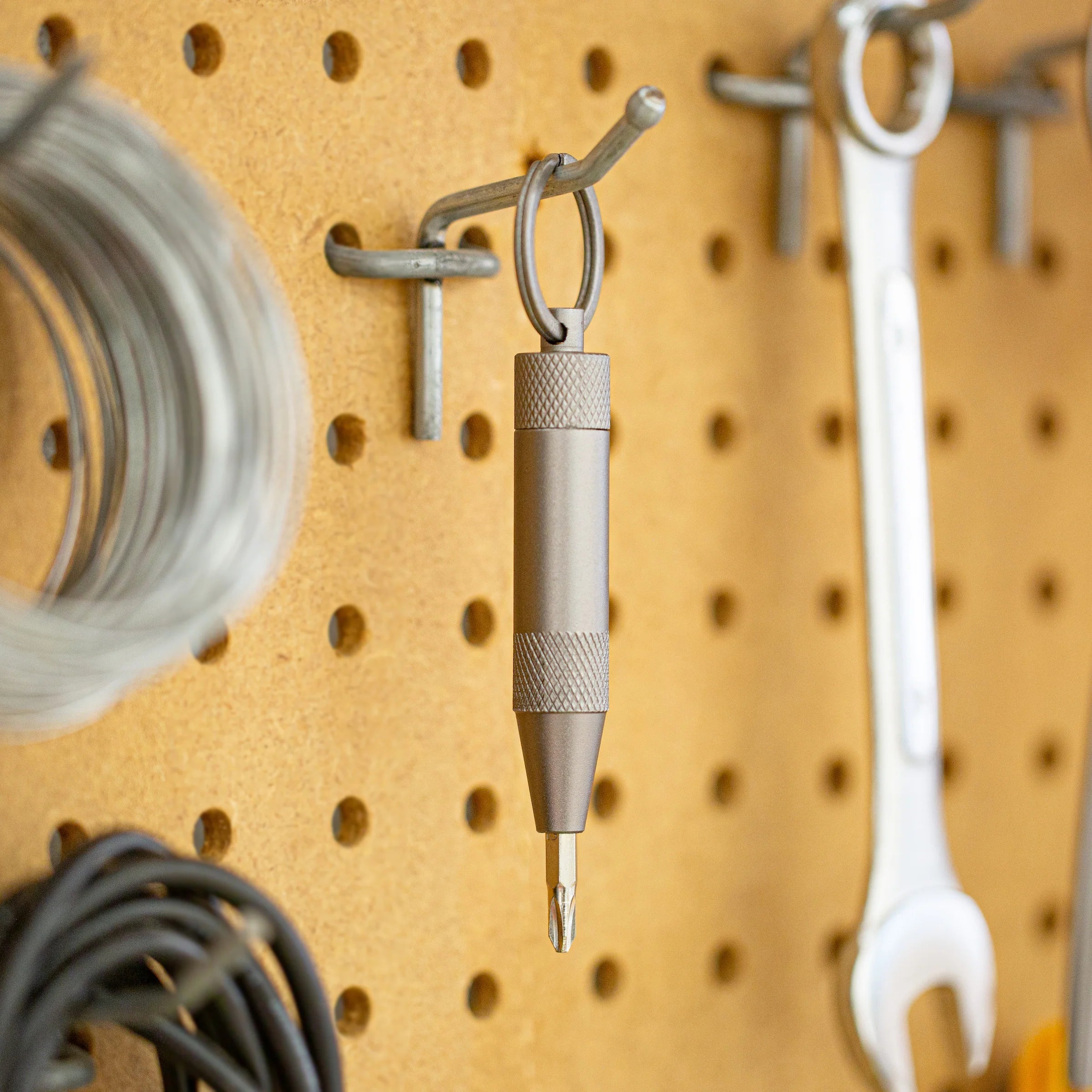 Metal mini screwdriver with a hook on a pegboard with various tools hanging on it.
