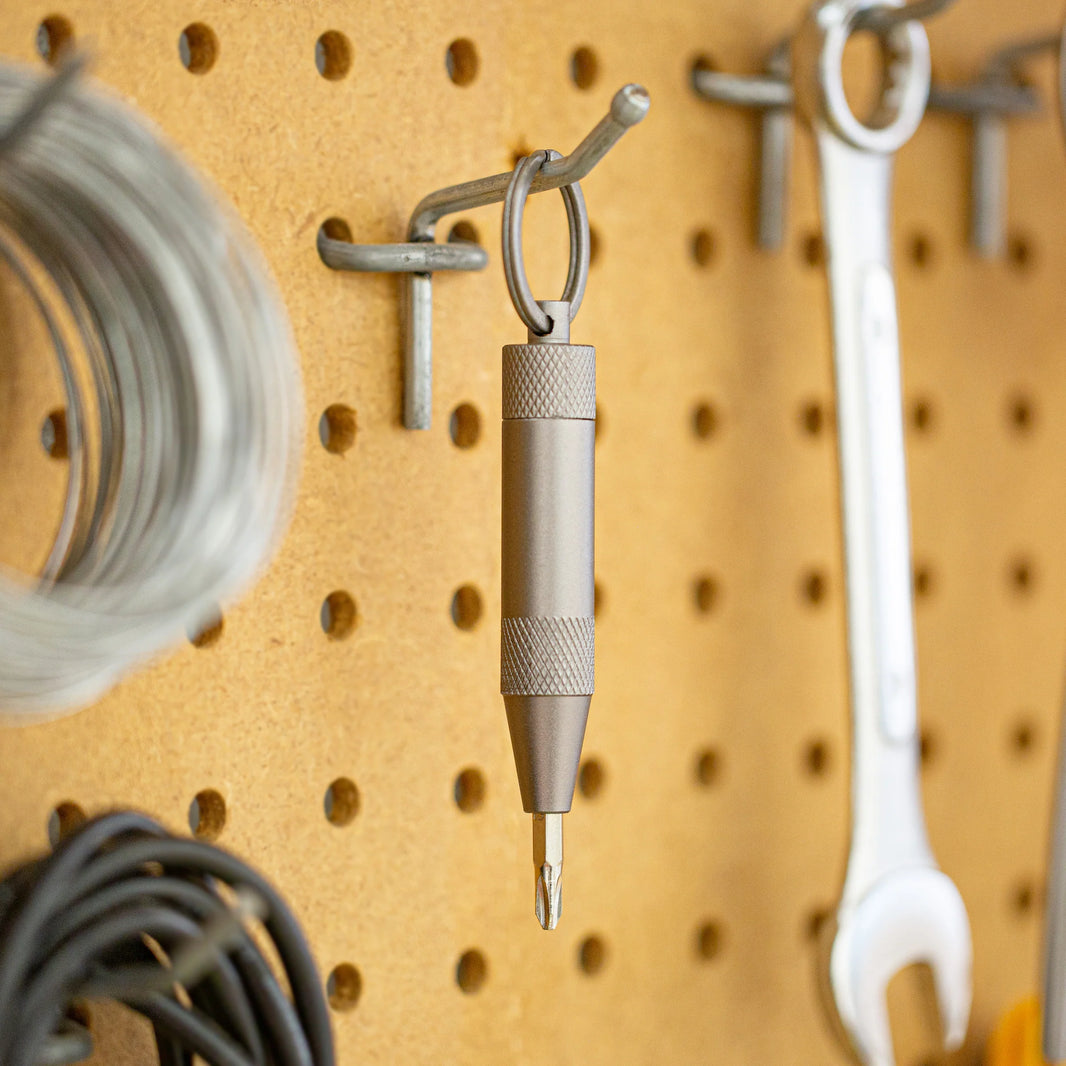 Metal mini screwdriver with a hook on a pegboard with various tools hanging on it.
