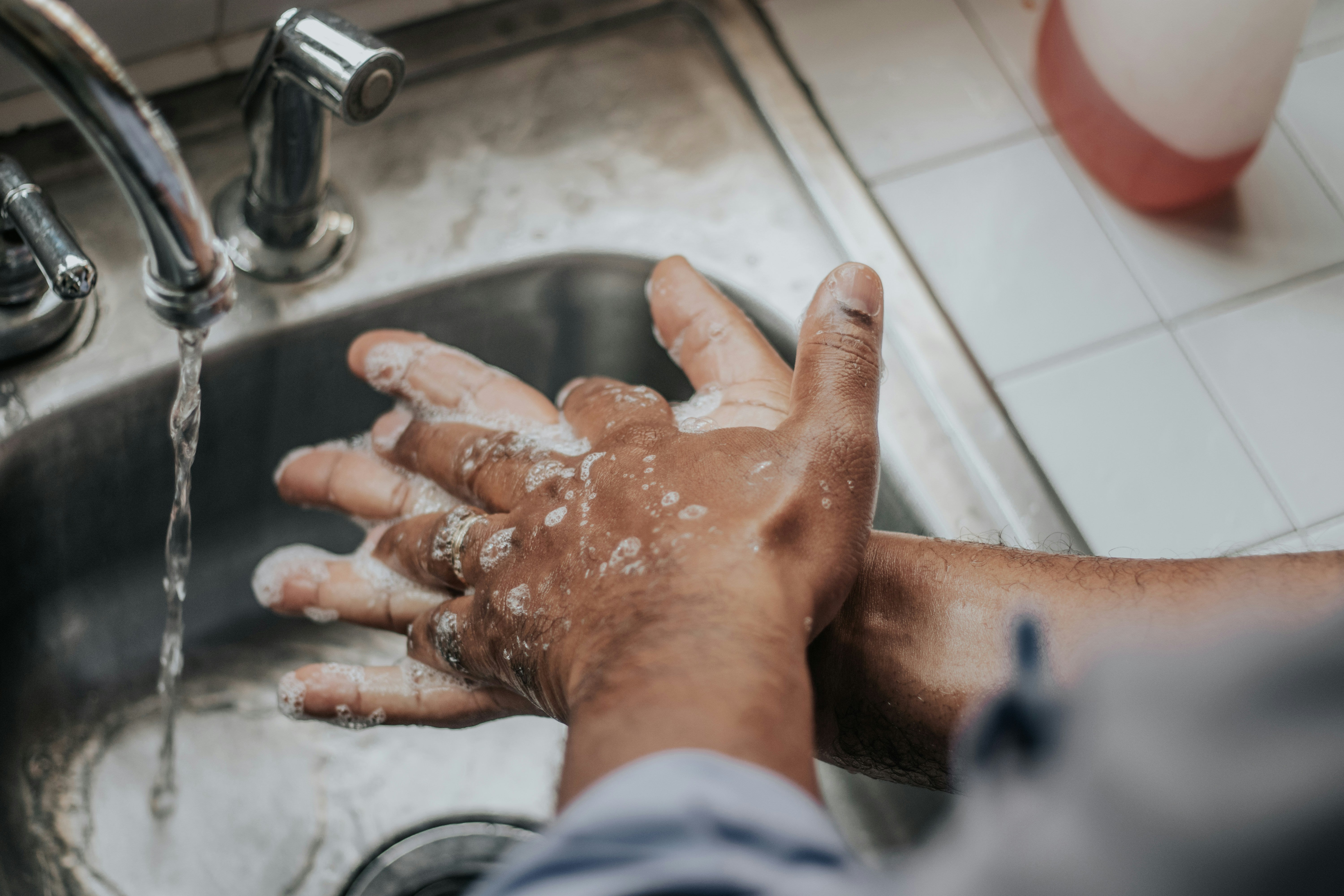 Person washing hands under running water in a sink.