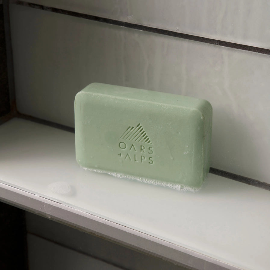 A bar of Oars and Alps Epsom Salt soap sitting on a white shelf.