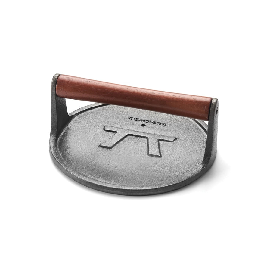 A round cast iron grill press with a wooden handle, featuring the Outset brand logo.