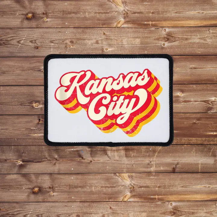 An iron on patch with the Kansas City Chiefs logo in red, yellow, and white colors on a wooden background.