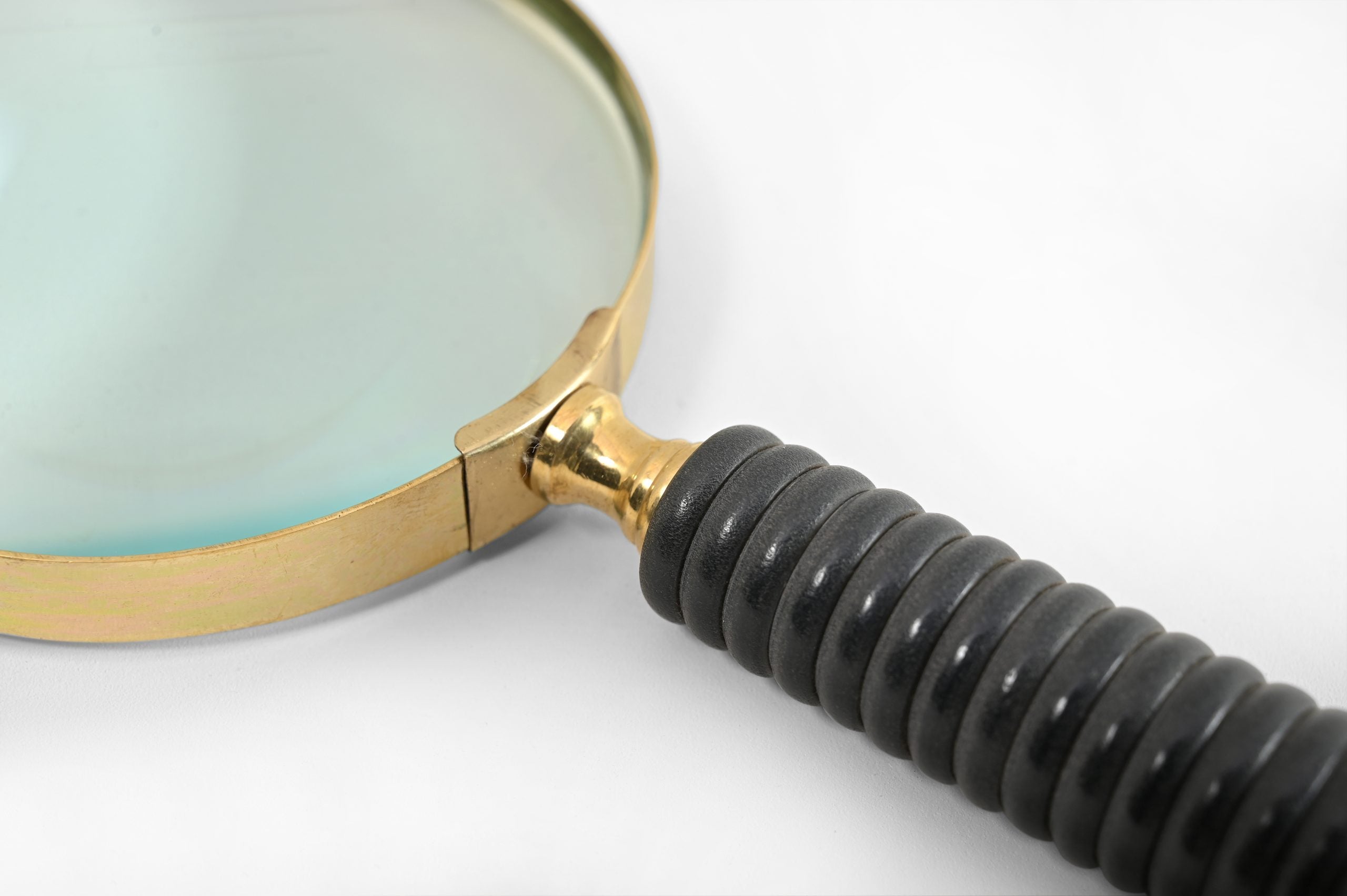 A close up of a magnifying glass with a black ribbed handle on a white background.