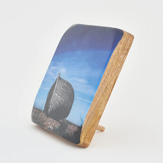 A decorative item featuring a black and white image of a beached traditional fishing boat on a wooden block.