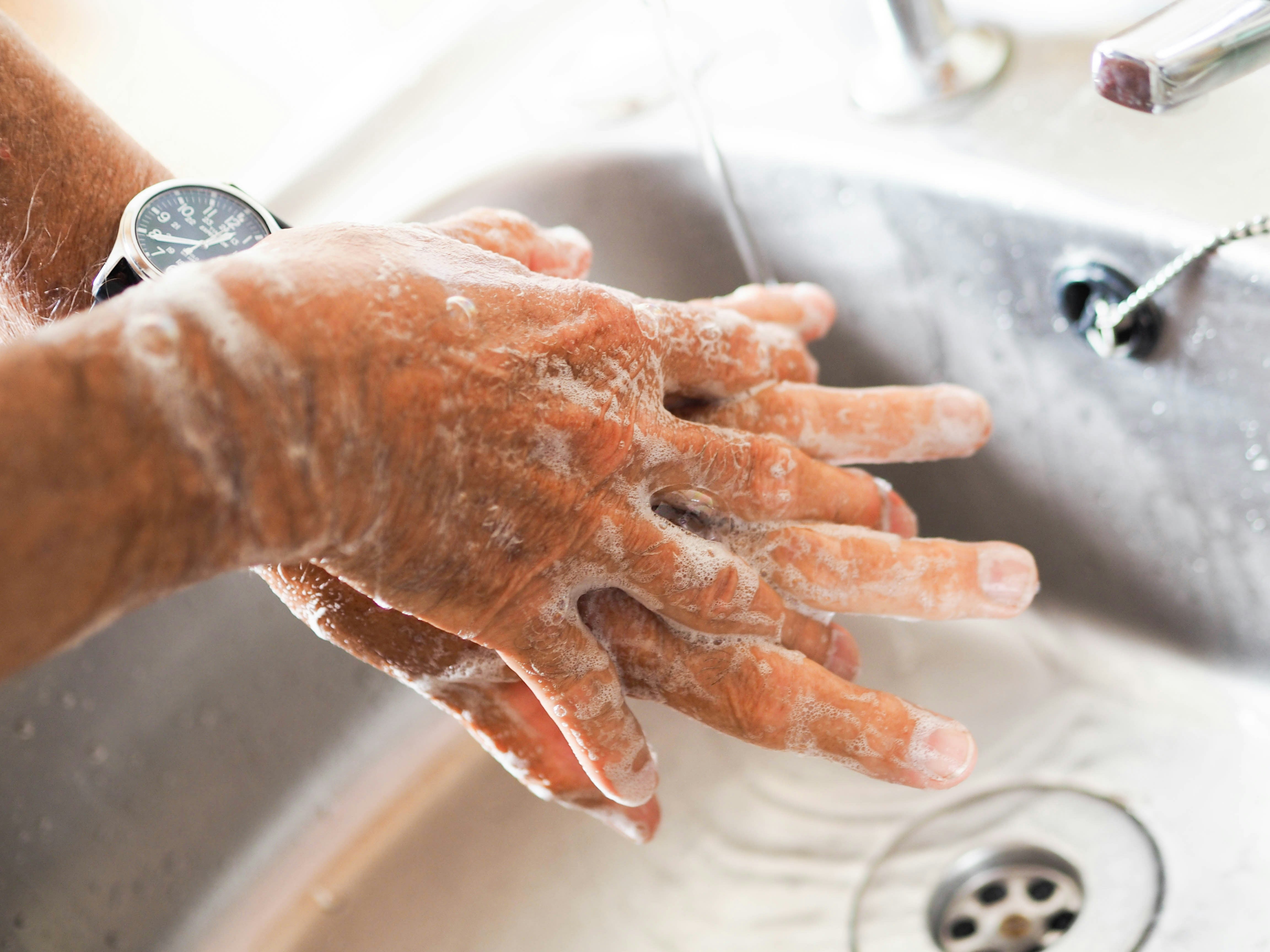 Person washing hands with soap under running water in a sink
