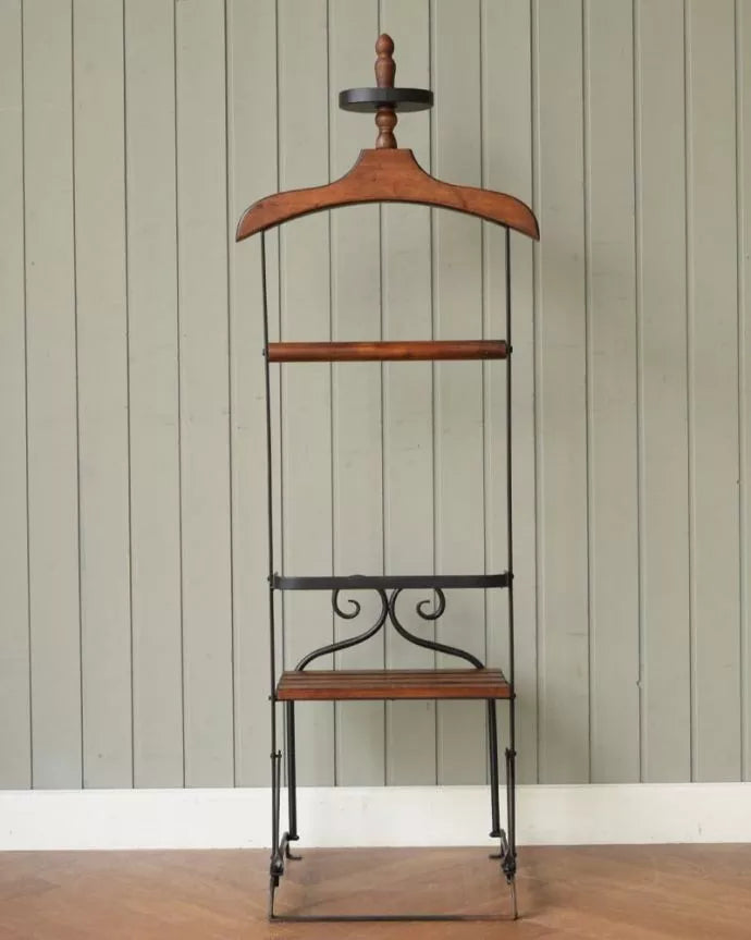 A clothing valet stand made of wood and metal, set against a wall.