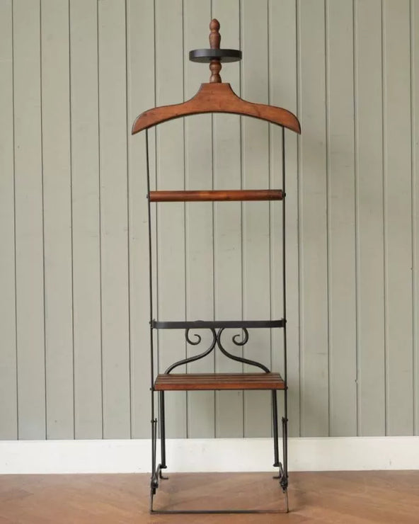 A clothing valet stand made of wood and metal, set against a wall.
