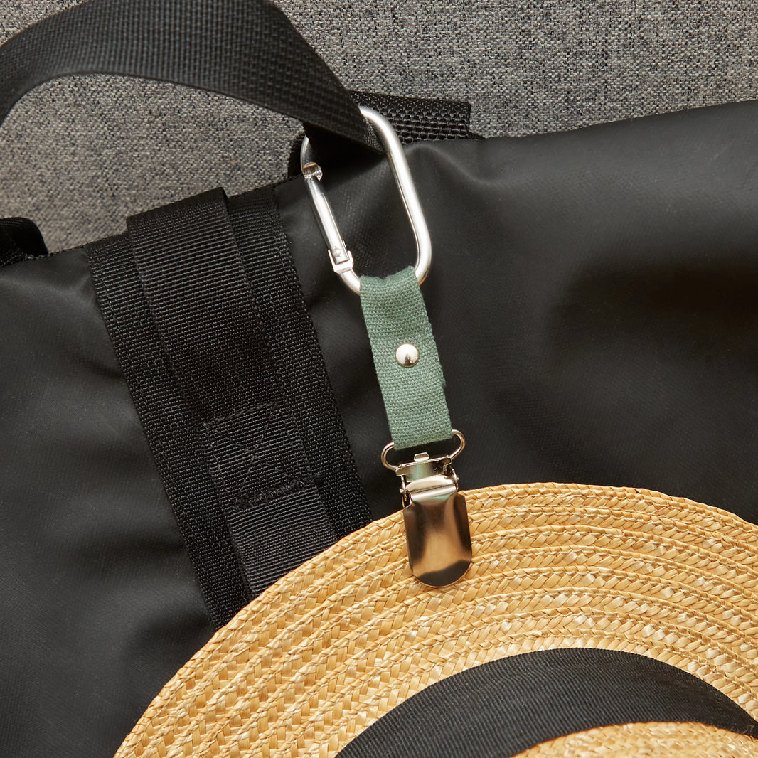 Straw hat with a green strap and carabiner attached to a black bag.