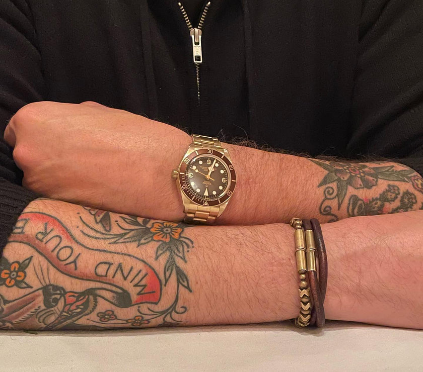 A man with tattoos wearing a watch on one hand and two leather bracelets on the other hand.