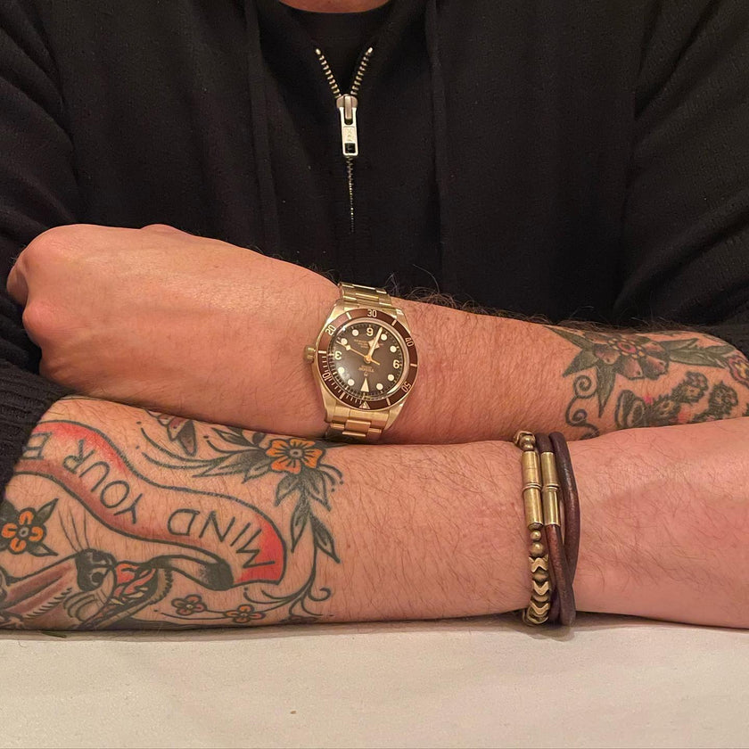 A man with tattoos wearing a watch on one hand and two leather bracelets on the other hand.
