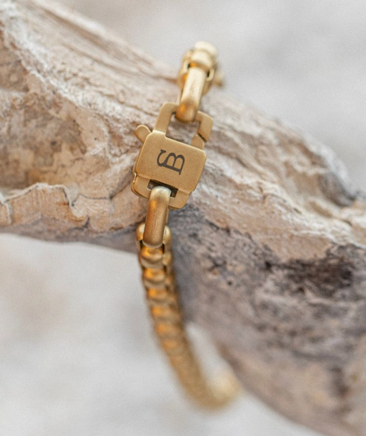 A close up of a gold bracelet's clasp featuring an 'SB' logo