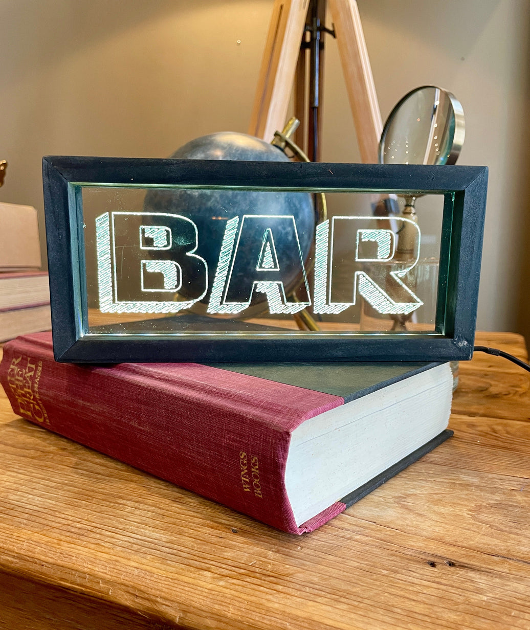 Decorative sign with 'BAR' on a stack of books on a wooden surface