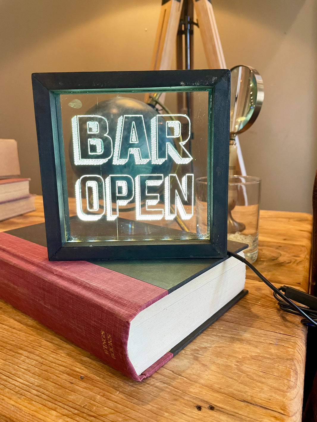 Lighted sign on a book that reads 'BAR OPEN' on a wooden surface.