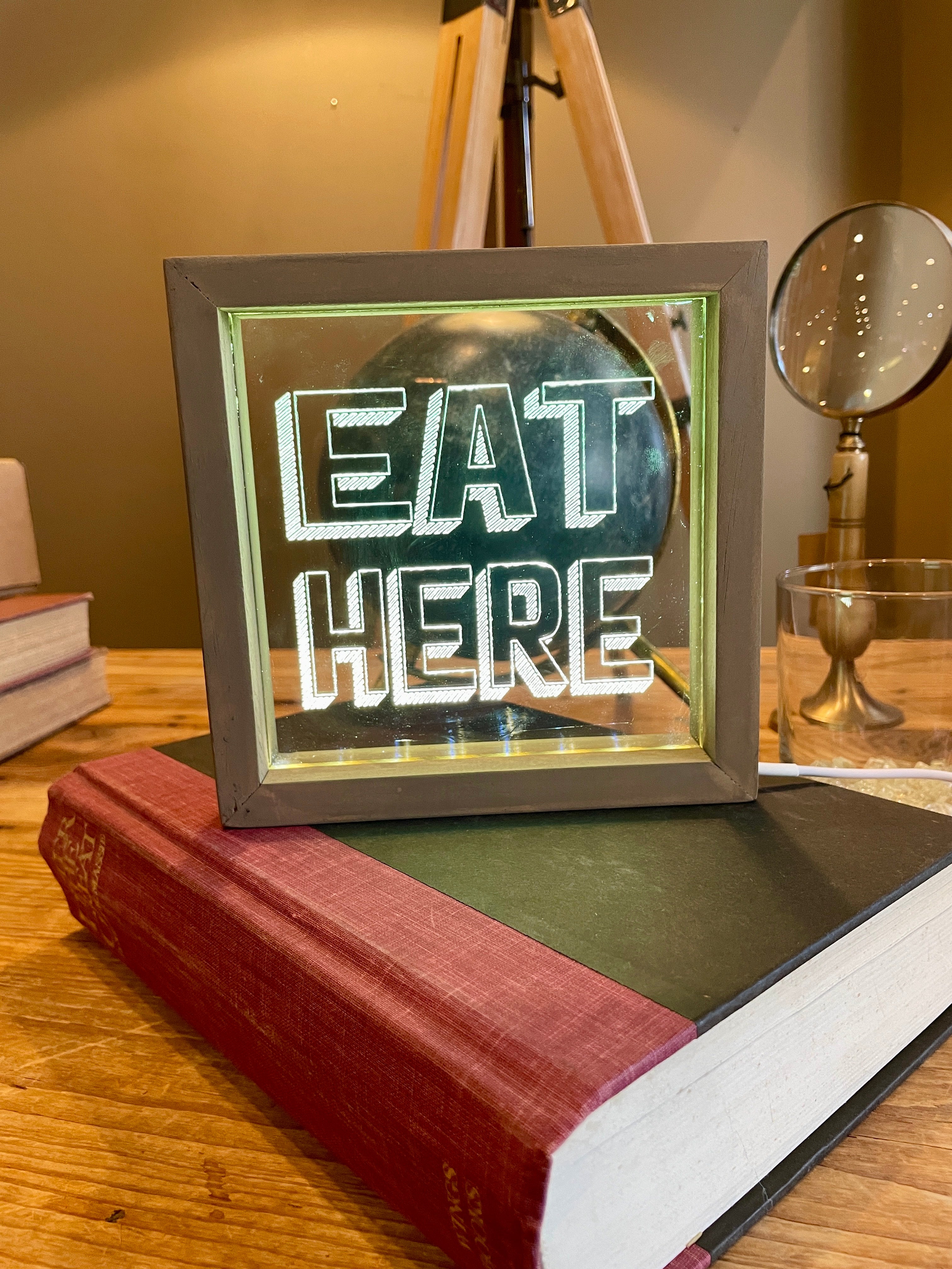 Light up sign with 'EAT HERE' text on a wooden surface