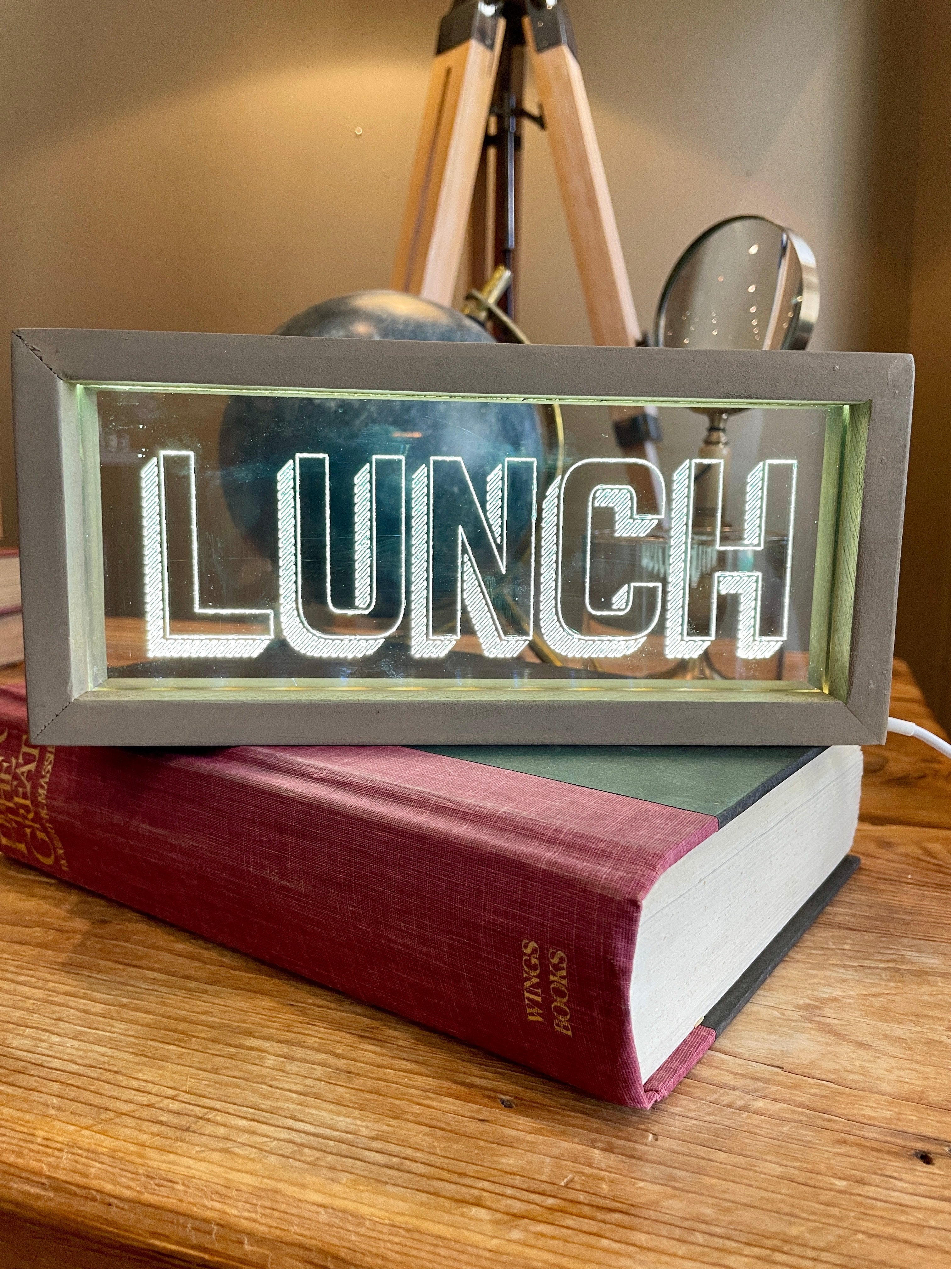 Lighted 'lunch' sign on a book on a wooden table.