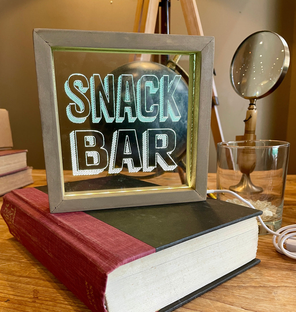 Decorative lighted sign with 'SNACK BAR' text on a stack of books.