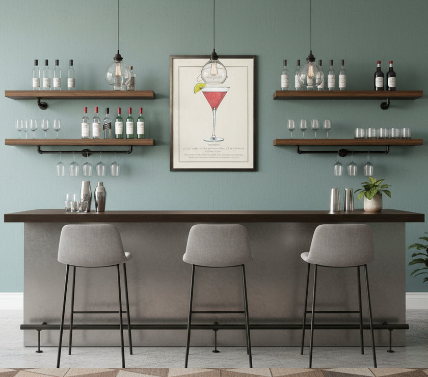 A watercolor art print of a cosmopolitan drink with recipe on a wall with shelving containing bottles and glasses with a bar and modern bar seating, a few potted plants nearby.