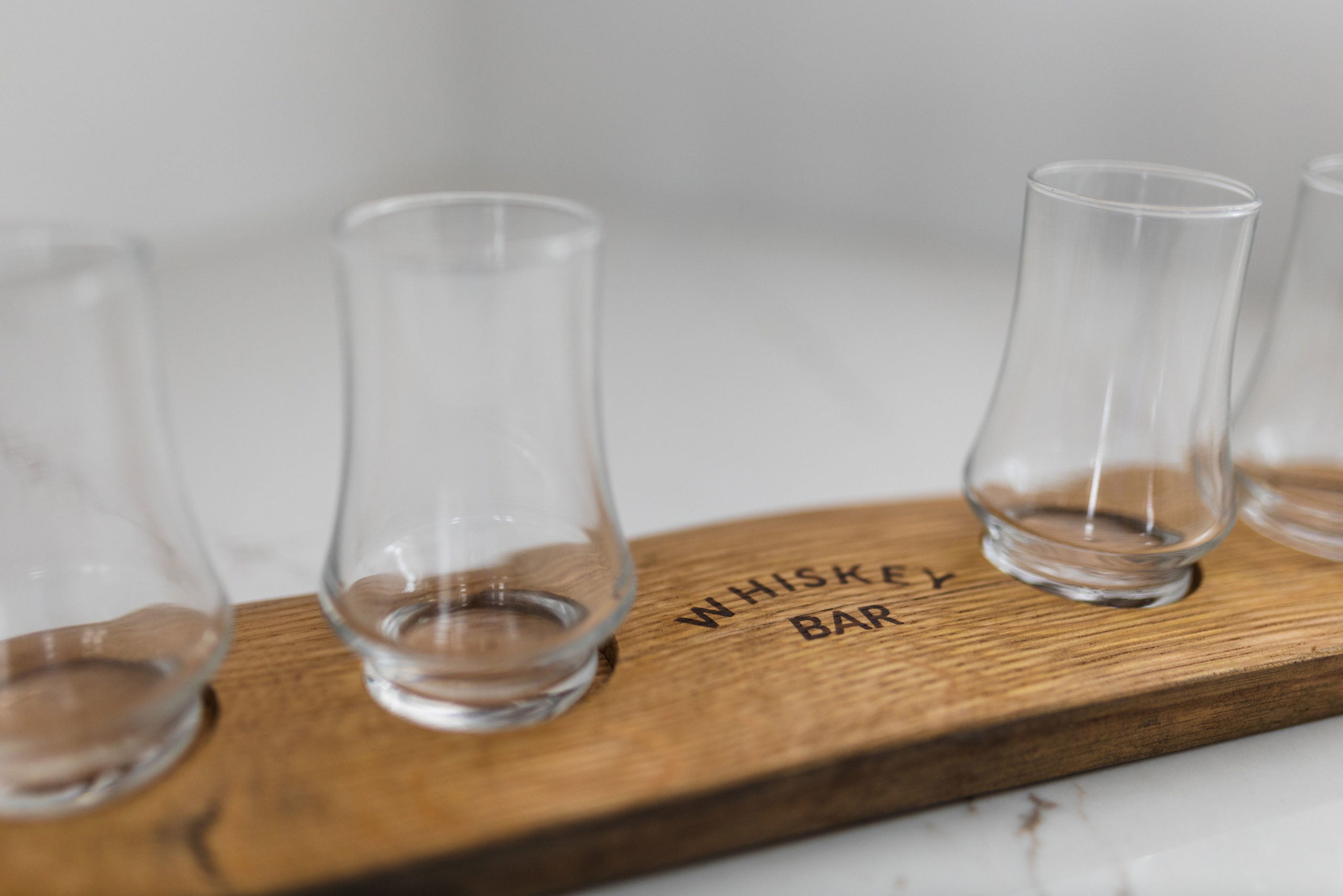 A closeup of a whiskey stave crafted tasting flight with glasses and 'whiskey bar' burned onto the wood.