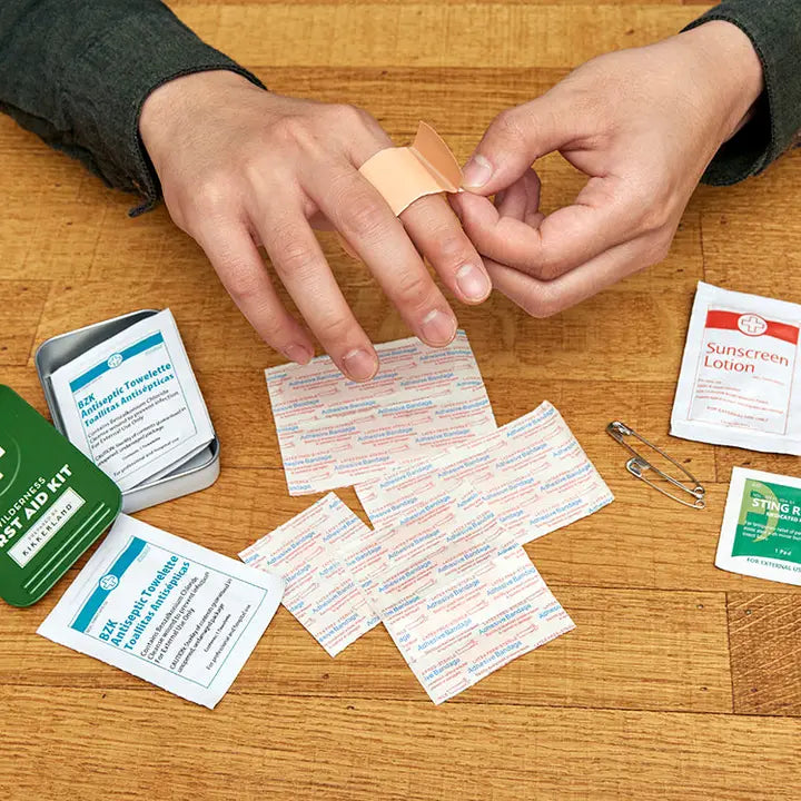 Person applying a bandage to a finger with a first aid kit on a wooden surface