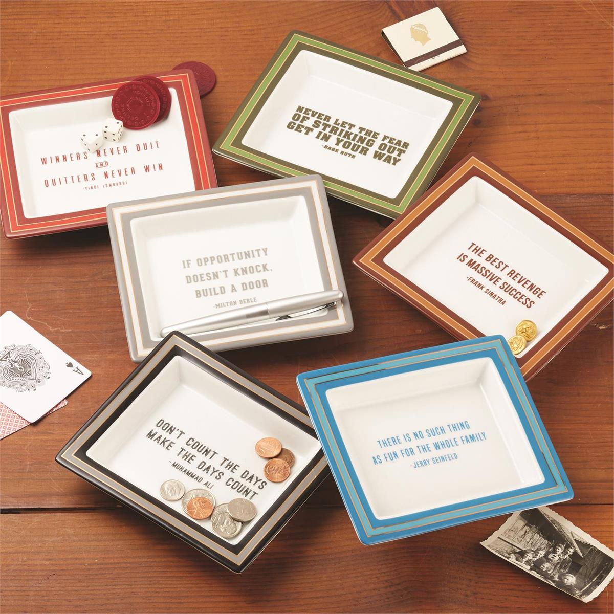 A collection of porcelain desk trays with various colorful frames and each featuring a different quote. They are displayed on a desk along with some coins and small decorative items.
