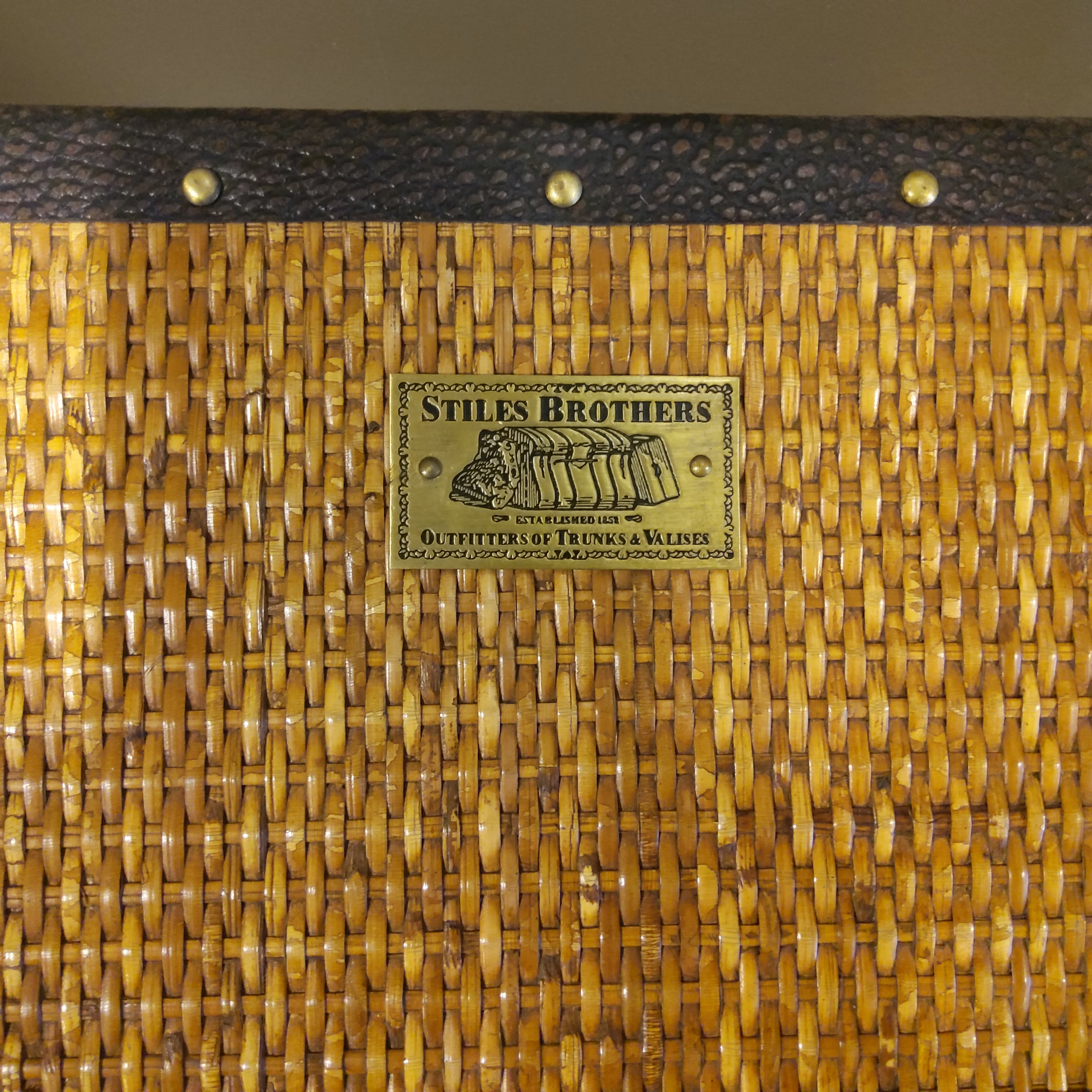 A close up of a campaign desk's maker label, which is metallic and stamped with Stiles Brothers, Outfitters of Trunks and Valises.