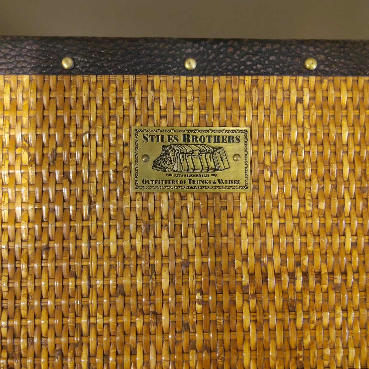 A close up of a campaign desk's maker label, which is metallic and stamped with Stiles Brothers, Outfitters of Trunks and Valises.