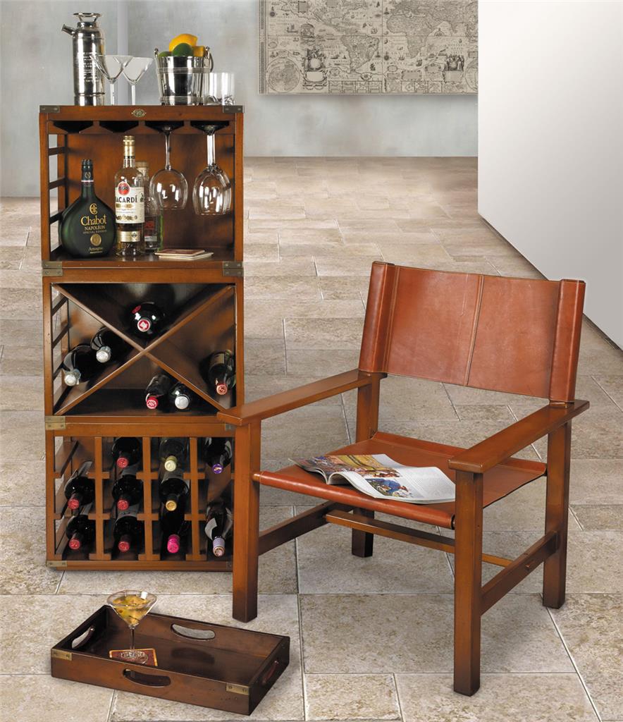 A wooden wine shelving unit containing bottle of twne, wine glasses, and barware, with a chair nearby with an open magazine on it.