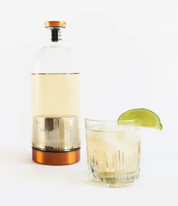 Infusion vessel with liquid inside next to a drink glass with a lime wedge on its rim.