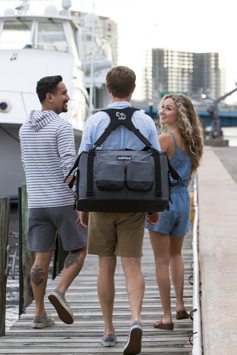 A person carrying a gray Ice Mule Traveler soft cooler with friends on a dock.