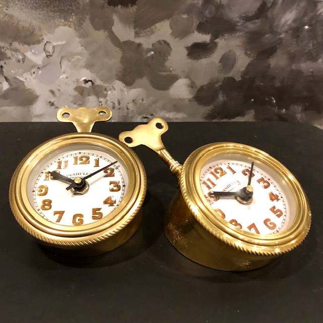 Two  golden colored table clocks with a wind up key in the back on a black surace.
