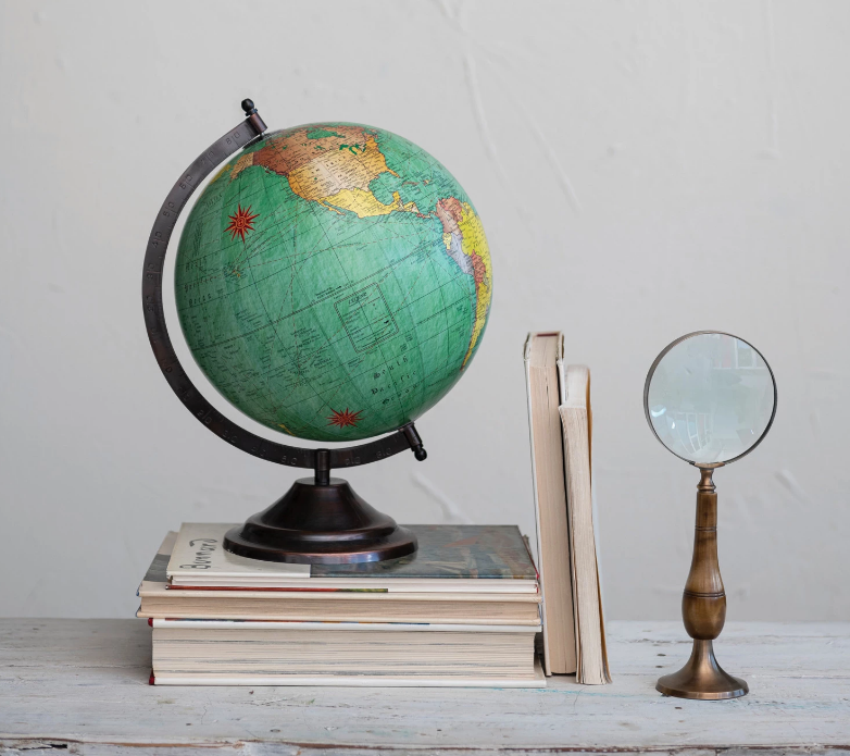 Vintage-style magnifying glass that acts as its own stand beside a stack of books with a globe set on top of the books.