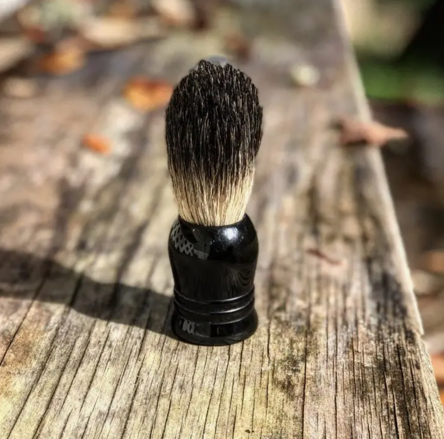 A boar hair shaving brush sitting on a wooden table outdoors.