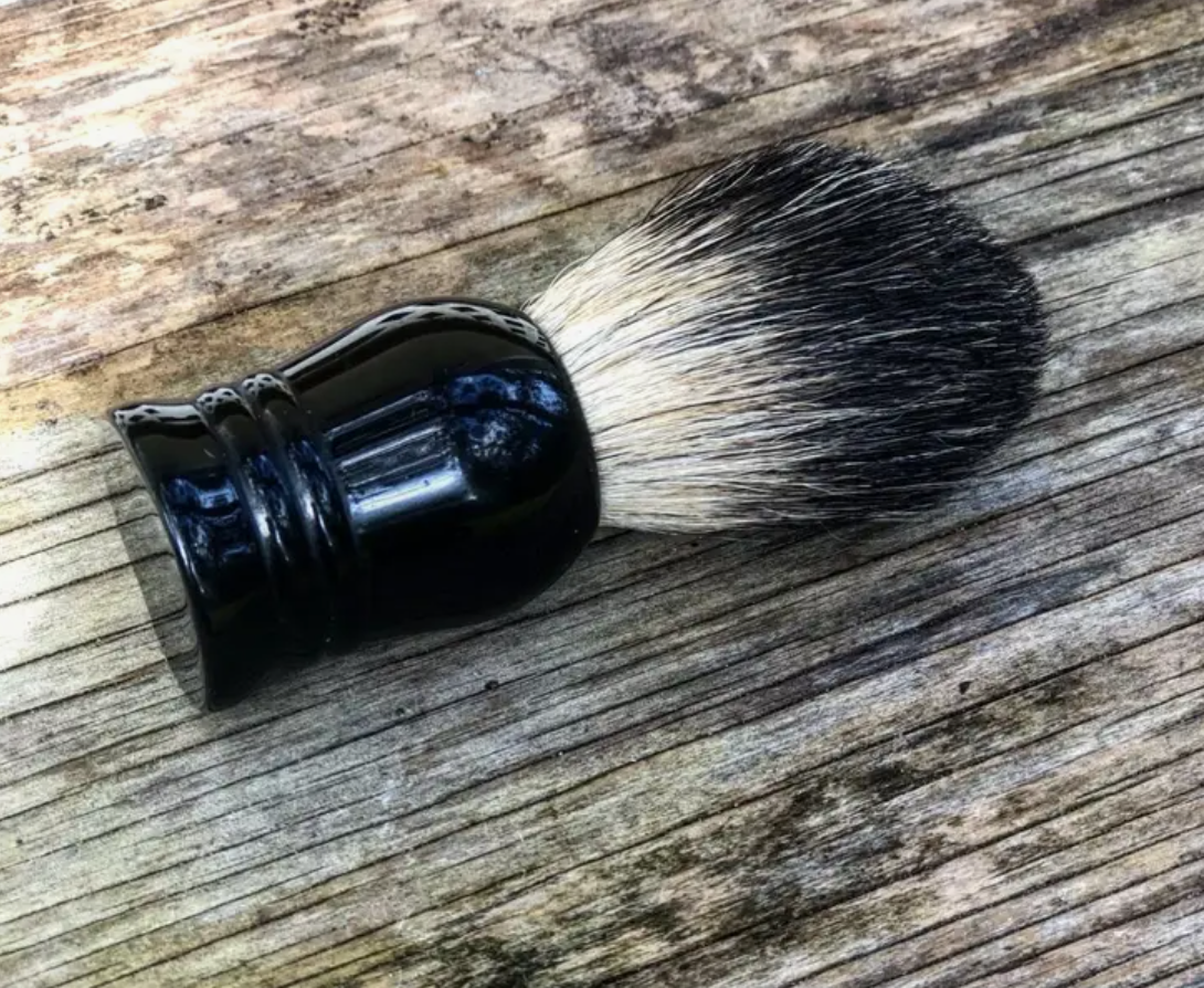 A boar's hair shaving brush with a black handle lying on a wooden surface.