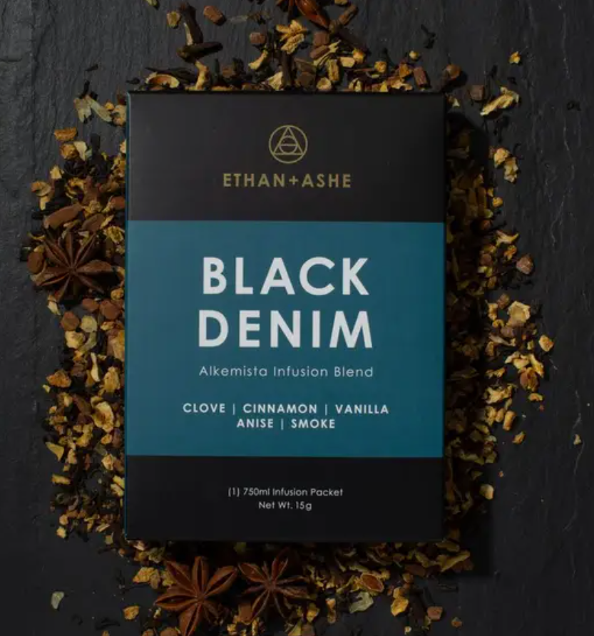 A package of 'Black Denim' Alkemista Infusion Blend by Ethan+Ashe with ingredients like clove, cinnamon, vanilla, and black cardamom displayed on a dark background.